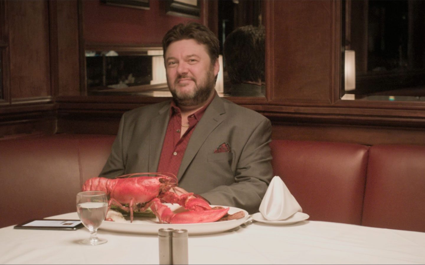 Man in a gray blazer and red shirt seated at a booth with a large lobster on a plate in a fine-dining restaurant. | Jerad Schutt | Nashville Marketing Consultant | Fractional CMO | Jerad Schutt | Nashville Marketing Consultant | Fractional CMO