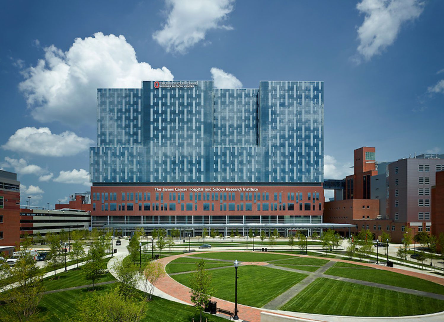 The James Cancer Hospital and Solove Research Institute building with red brick base and tall blue glass towers against a blue sky with clouds. | Jerad Schutt | Nashville Marketing Consultant | Fractional CMO | Jerad Schutt | Nashville Marketing Consultant | Fractional CMO