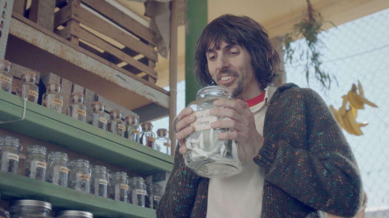 Man in a cardigan holding a glass jar with a handwritten label in a market aisle. | Jerad Schutt | Nashville Marketing Consultant | Fractional CMO | Jerad Schutt | Nashville Marketing Consultant | Fractional CMO