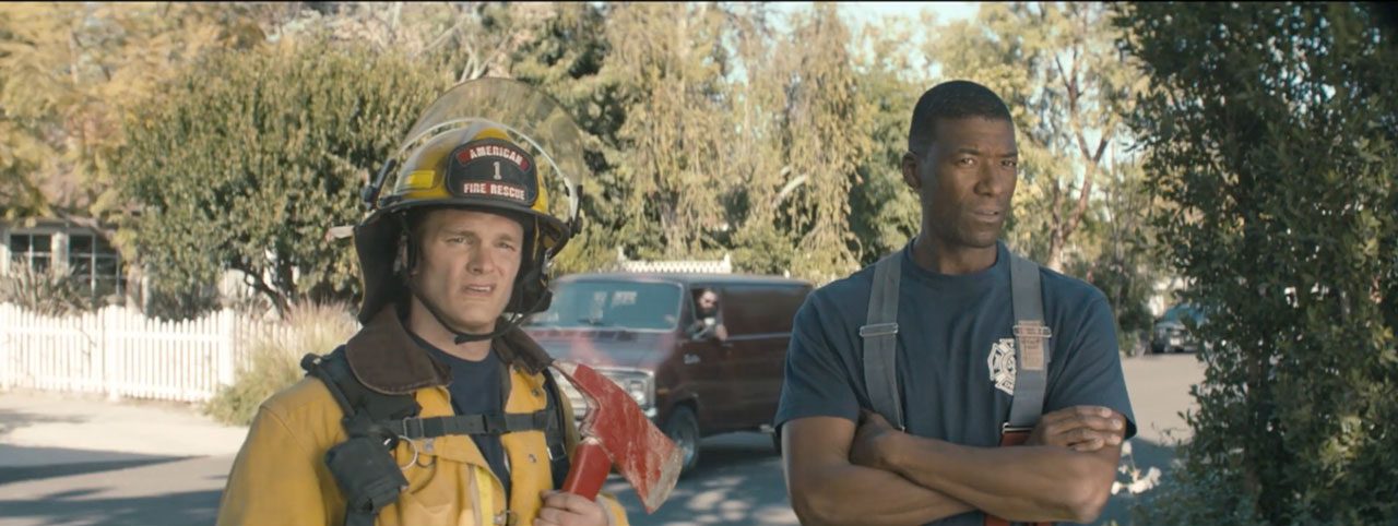 Two firefighters stand on a suburban street, one in yellow turnout gear holding an axe and wearing a helmet, the other in a blue uniform with arms crossed. | Jerad Schutt | Nashville Marketing Consultant | Fractional CMO | Jerad Schutt | Nashville Marketing Consultant | Fractional CMO