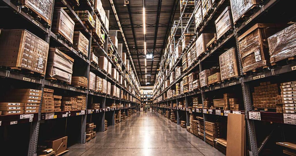Aisle in a warehouse with tall metal shelves stacked with cardboard boxes and pallets in rows,. | Jerad Schutt | Nashville Marketing Consultant | Fractional CMO | Jerad Schutt | Nashville Marketing Consultant | Fractional CMO