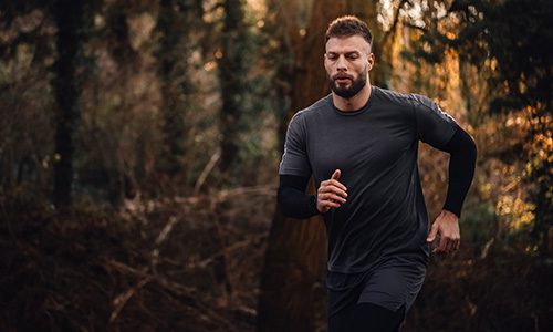Man with a beard jogging on a forest trail at dusk in dark athletic wear. | Jerad Schutt | Nashville Marketing Consultant | Fractional CMO | Jerad Schutt | Nashville Marketing Consultant | Fractional CMO