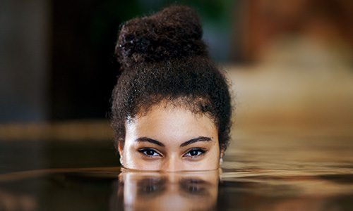 Close-up of a woman's eyes and hair bun above water, with her reflection on the water surface. | Jerad Schutt | Nashville Marketing Consultant | Fractional CMO | Jerad Schutt | Nashville Marketing Consultant | Fractional CMO