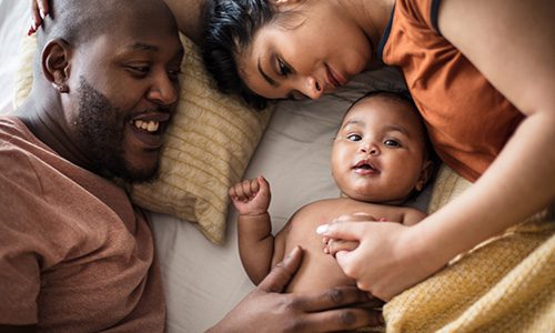 Parents and their baby lie on a bed, smiling and cuddling close for a warm family moment. | Jerad Schutt | Nashville Marketing Consultant | Fractional CMO | Jerad Schutt | Nashville Marketing Consultant | Fractional CMO